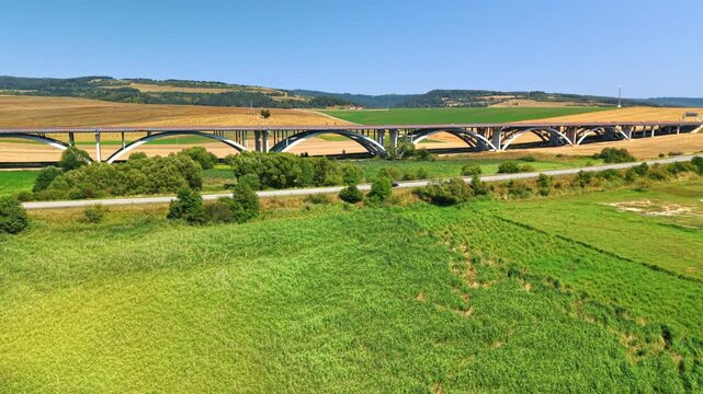Multi span viaduct built over green field in Slovakia. Concrete arch highway bridge standing over grassy land under sunny sky.