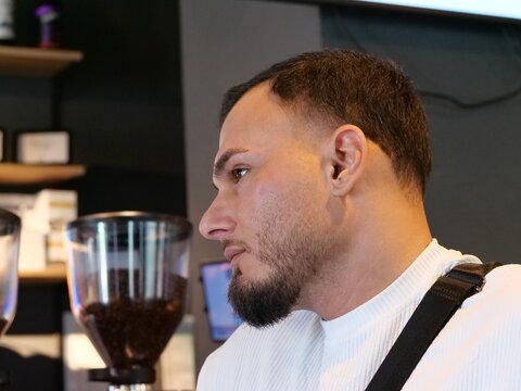 Side Profile Portrait of a Young Man with Beard Looking Away inside a Trendy Urban Coffee Shop Environment