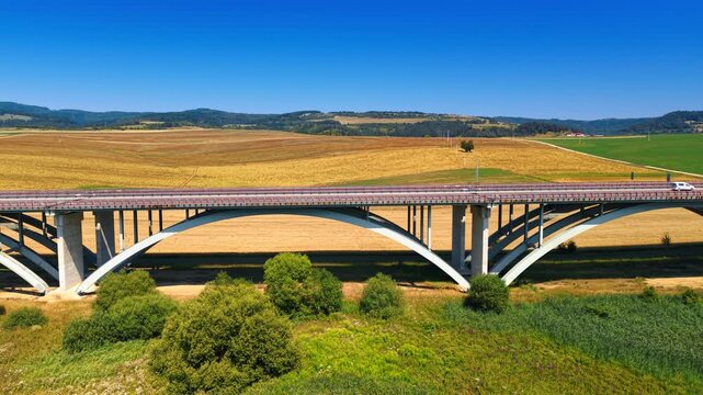 Tall support structures of highway viaduct in Slovakia. Highlights concrete arches of bridge against background of yellow field.