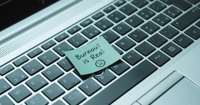 Person places a &ldquo;Burnout is Real&rdquo; sticky note on a laptop keyboard and closes the computer, concept of work stress, exhaustion, burnout and need for rest.