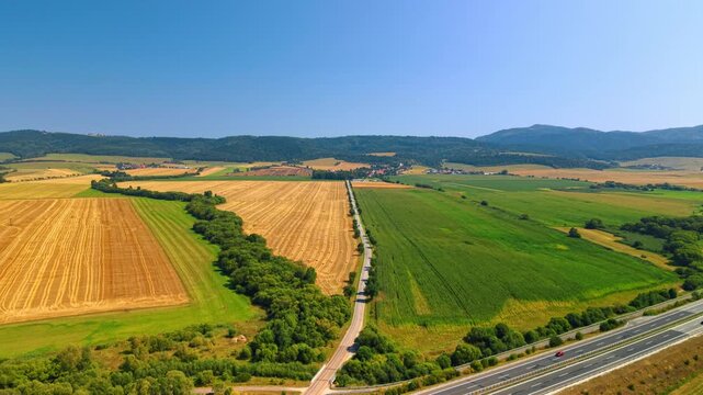 Agricultural landscape with colorful patchwork fields. Aerial photograph shows yellow harvested land, green crops and rural asphalt road under clear sky.