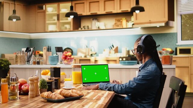 Woman freelancer uses green screen laptop while solving daily tasks, multitasking and telecommuting in wireless hybrid work for productivity at home.