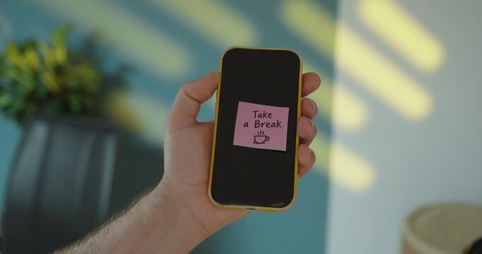 Hand holding smartphone with &ldquo;Take a Break&rdquo; sticky note, concept of digital detox and screen time break