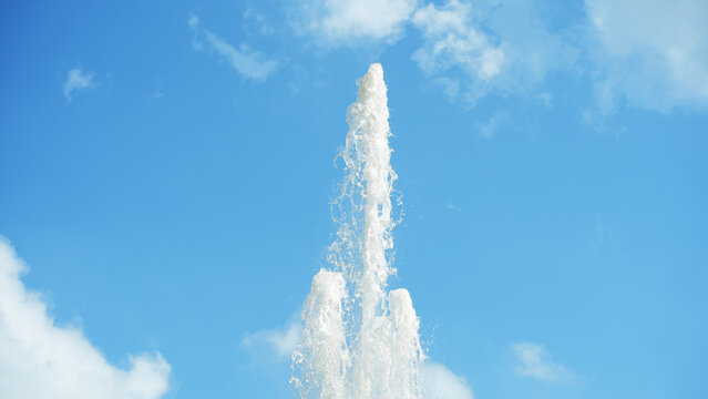 High water jet of a fountain against blue sky with clouds