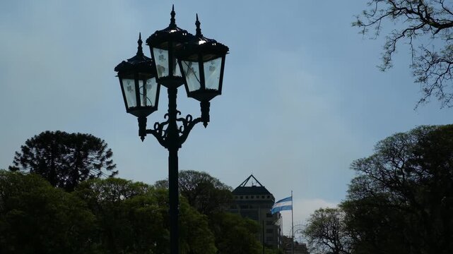 A classic street lamp stands in a sunny park with trees and a national flag