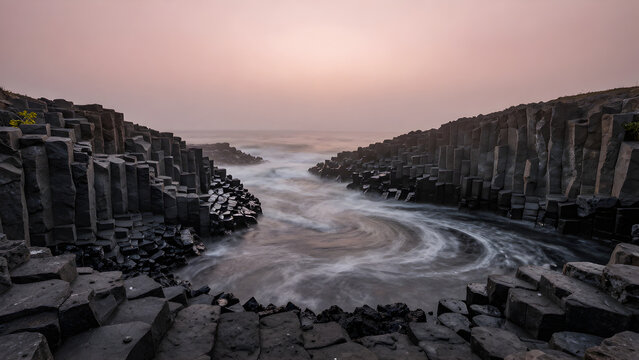 Seascape waves crashing between dark rock formations at sunrise