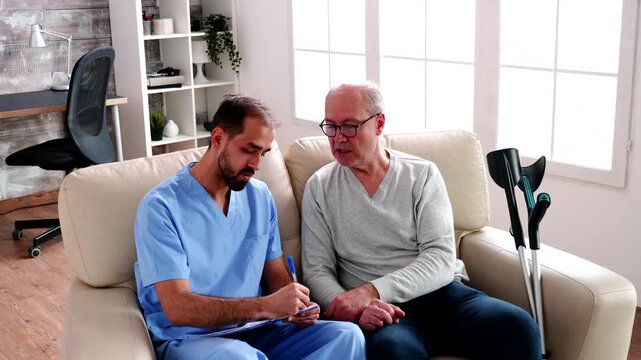 male healthcare worker takes clipboard notes beside an older man, showing one-to-one consultation, care documentation and supportive communication, also emphasizing wellbeing and assessment.