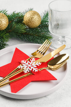Holiday table setting with golden cutlery arranged in red star shaped cutlery holder decorated with white snowflake on white plate, showy Christmas tree branch on light textured background