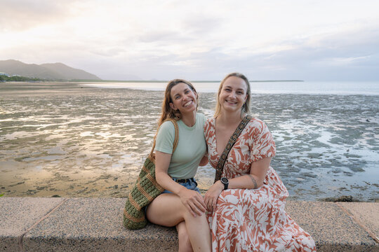 Two happy women sitting side by side on a stone ledge overlooking the coastal landscape