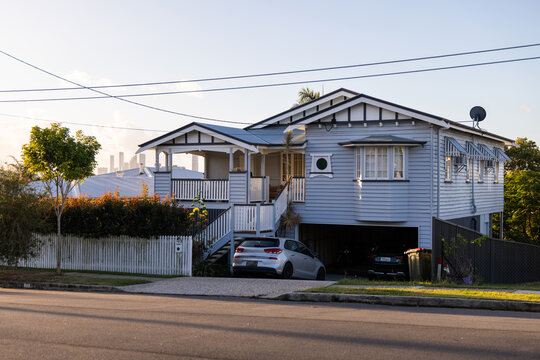 Streetview of an elevated home painted in soft blue-grey with crisp white trim and gabled roof