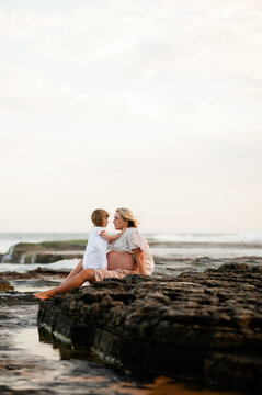 Mother and child bonding on rocky beach during sunset with gentle waves in background