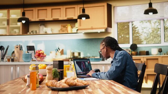 Young adult edits photograph on laptop for post production, using image processing, retouching, color grading software and graphic design skills.