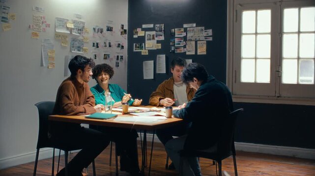 Creative production team sitting around meeting table, discussing script layouts and storyboards in studio with reference boards on walls