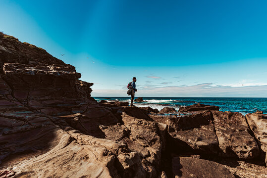 man with backpack standing on rugged coastal rocks
