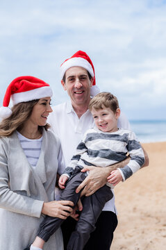 Happy family celebrating Christmas at the beach with Santa hats and joyful expressions