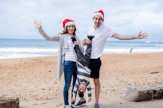 Family joyfully celebrating Christmas on the beach, wearing Santa hats