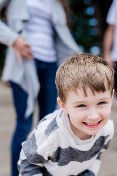 Young boy with short hair smiling while playing outdoors, family visible in background