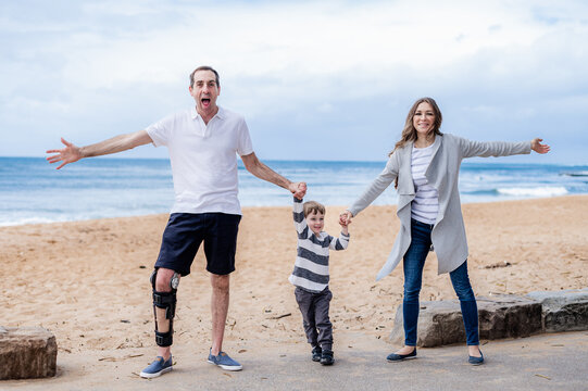 Family captures joyful moment at the beach, holding hands and smiling near ocean waves