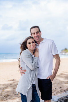 Couple stands together with smiles, enjoying their time at the beach on a cloudy day