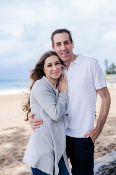 Couple standing closely together on sandy beach with ocean in the background