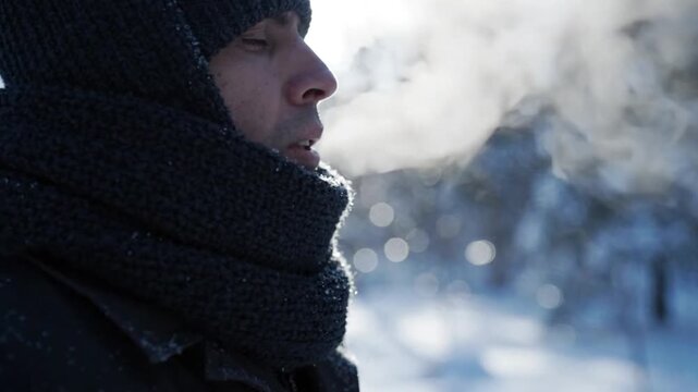 Close up profile of a young man breathing out visible steam in freezing cold winter weather outdoors.