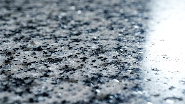 Macro shot of polished grey granite stone texture with bright light reflection.