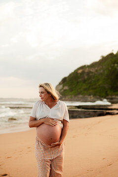 Expecting mother standing on beach at sunset, wearing casual clothing, peaceful mood