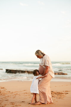 Expectant mother embraces child on beach at sunset