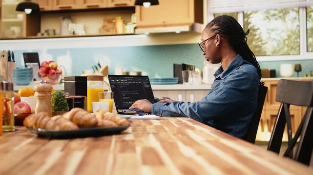 Person codes on laptop in kitchen during remote IT work, writing source code and using command-line tools for software development and engineering at home.