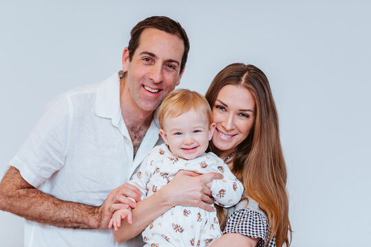 happy mid aged family of mid aged female mom and male dad holds up a young baby boy with blond hair