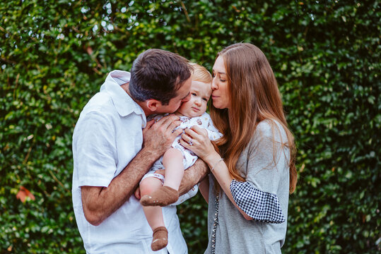 mid aged mother and father squishes young baby boy with blond hair  in front of a green background