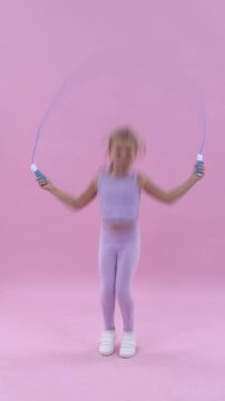 Cute little girl jumping with skipping rope on pink background