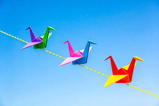 Colorful origami cranes flying in clear blue sky