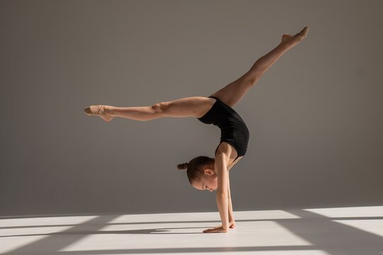 Little Caucasian girl gymnast in a black leotard posing on a white background. 