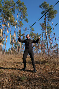 Young adult man performs resistance band exercise during outdoor fitness session in pine forest. Elastic training band black athletic clothing, healthy lifestyle, functional strength endurance