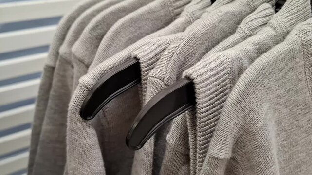 Row of warm grey knitted sweaters hanging on wooden hangers in a wardrobe. Fashion clothing, winter apparel, organized closet.