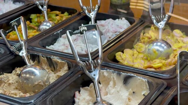 Close-up various fresh salads and sauces in black plastic containers with metal serving scoops at buffet counter inside restaurant. Catering food service, hospitality buffet display.