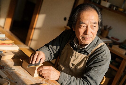 Senior woodworker sanding wooden block in workshop