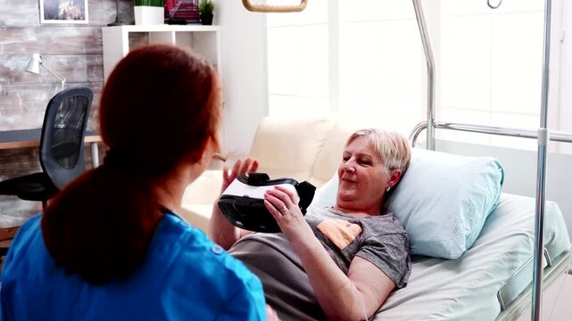 Nurse introducing virtual reality headset to senior woman in bed