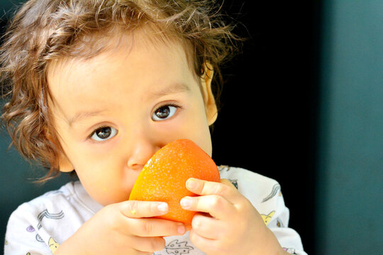 Cute toddler eating the quarter of orange.
