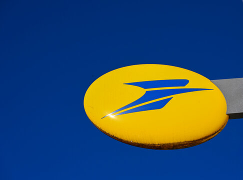enseigne de la poste en France, logo bleu et blanc sur un fond ovale jaune avec un ciel bleu en arri&egrave;re plan.