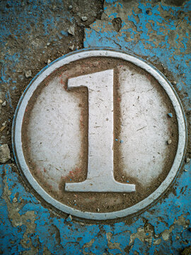 Metal number one disc embedded in weathered blue ground