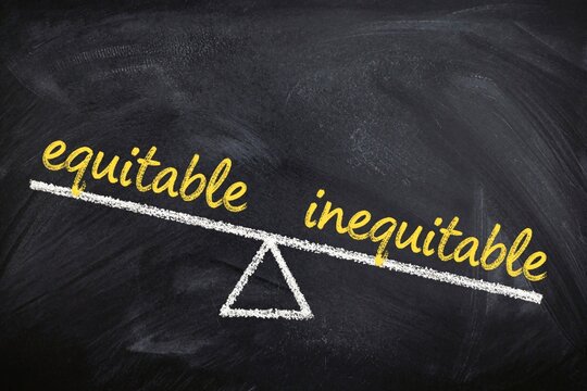 Chalk scales show imbalance between equitable and inequitable written on blackboard. Concept of fairness choice, justice and unfairness or bias.