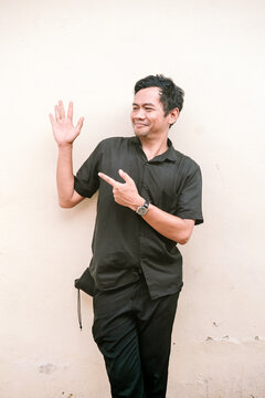Man in black shirt pointing and waving against light wall