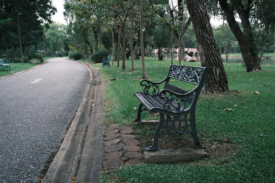 Empty ornamental metal bench beside a curving park road