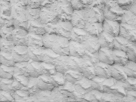 A detailed black and white texture of a rough uneven stone wall thickly covered with white stucco plaster, creating an abstract rustic grunge background for architectural and interior loft design.