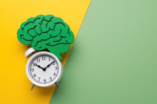 Green brain silhouette sits on top of white alarm clock. Conceptual mental health wellness imagery on yellow, green background. Symbolize cognitive function time management, mindfulness routine for