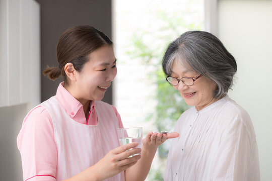 訪問介護で高齢者の服薬を支援する介護福祉士や看護師の女性ホームヘルパー、在宅介護、薬、服薬確認、水を渡すイメージ