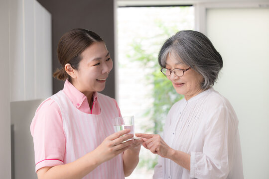訪問介護で高齢者の服薬を支援する介護福祉士や看護師の女性ホームヘルパー、在宅介護、薬、服薬確認、水を渡すイメージ