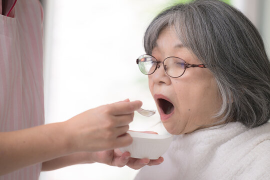 A close-up of the mouth of a female home health aide providing meal assistance to the elderly as part of in-home care&mdash;an image evoking the image of a female caregiver who supports eating 
